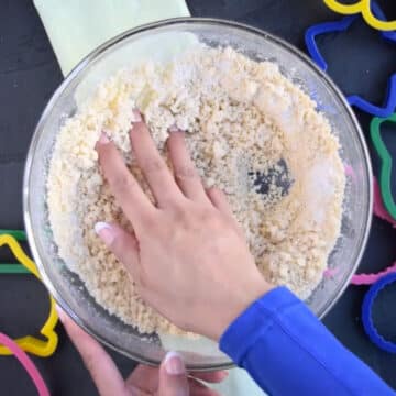 Hands being used to knead dough in glass bowl. 