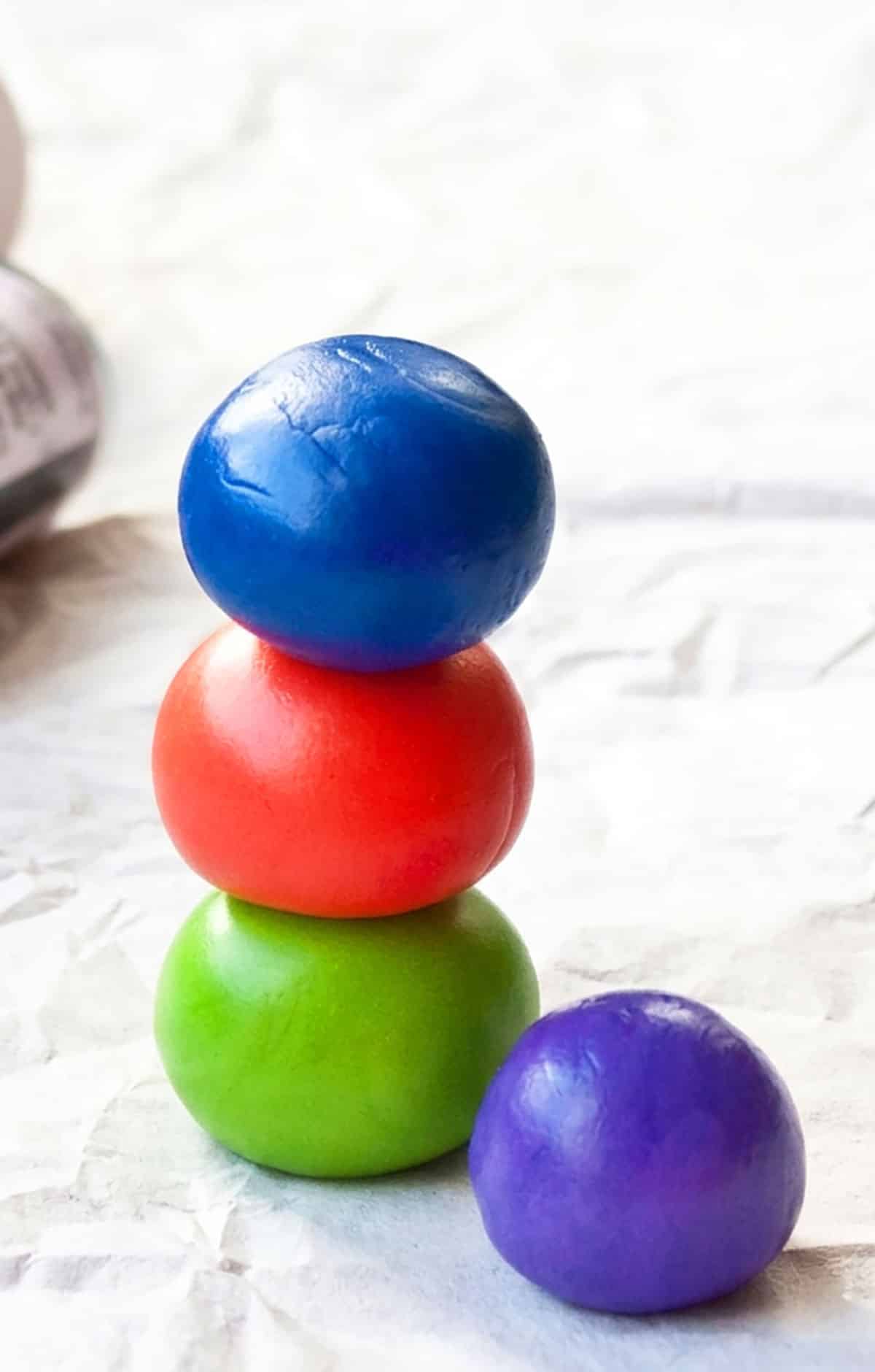 Tinted fondants balls stacked on top of each other on sheet of parchment paper. 