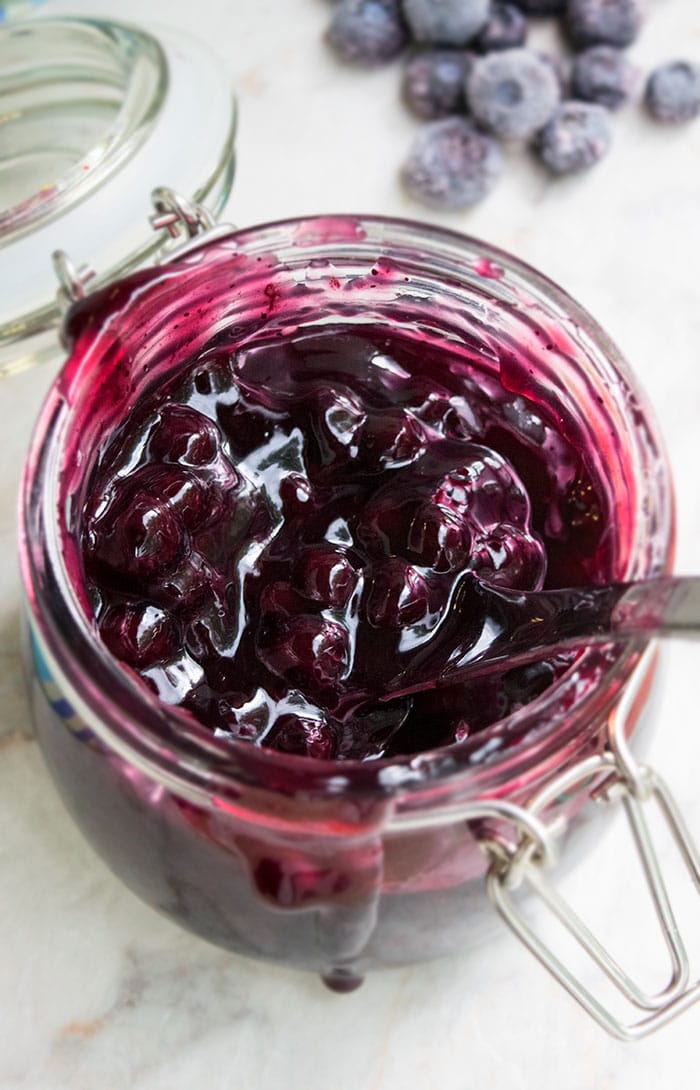 Easy Blueberry Pie Filling in Glass Jar on White Marble Background. 