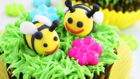 A homemade cakesicle decorated with edible bees in a bowl full of