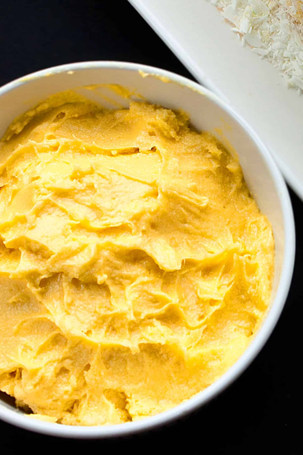 Mango buttercream frosting in white bowl. 