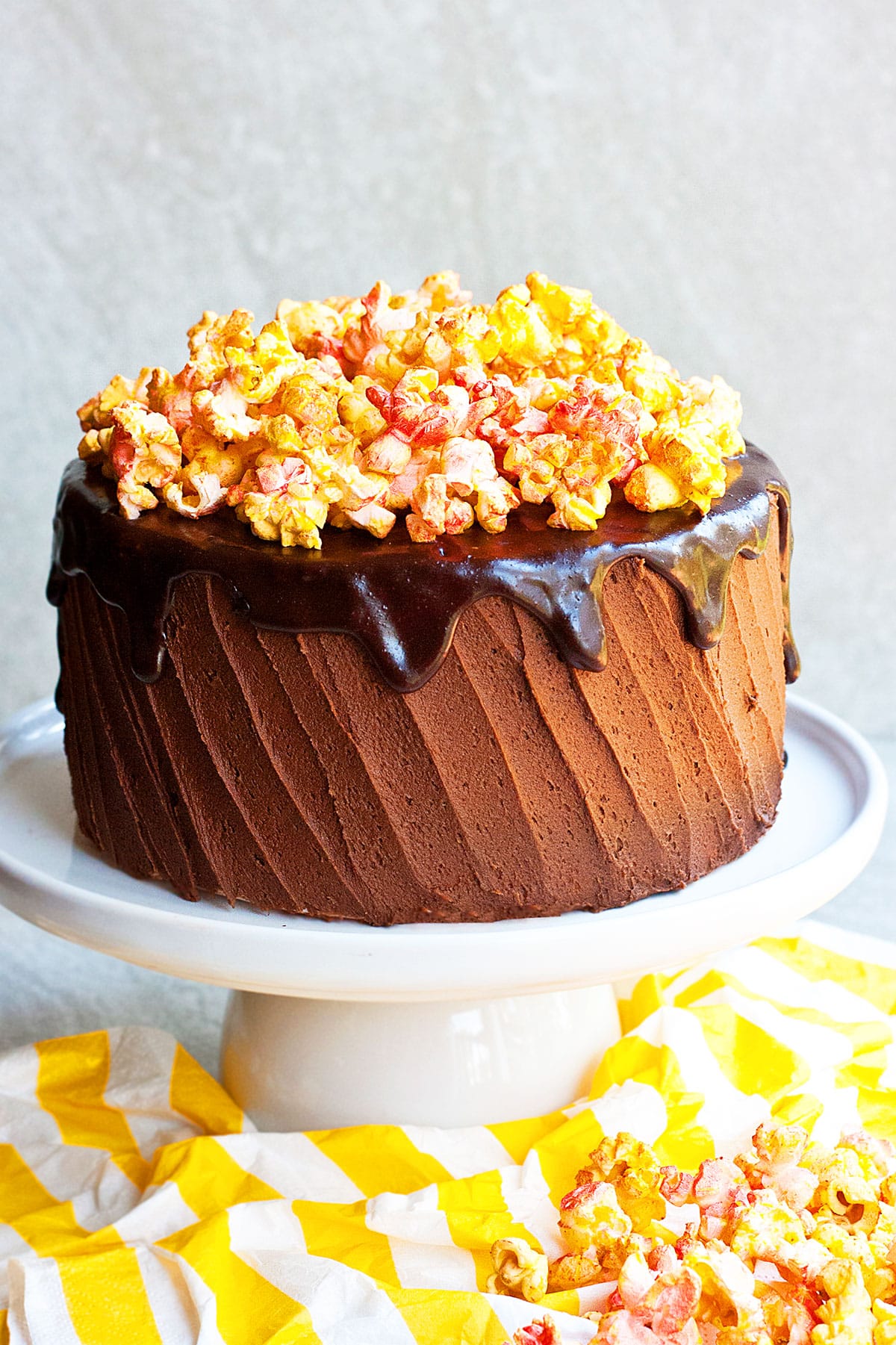 Easy soft and moist chocolate popcorn cake with chocolate buttercream frosting and chocolate ganache on white cake stand. 