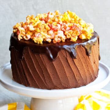 Easy soft and moist chocolate popcorn cake (layer cake) with chocolate buttercream frosting and chocolate ganache on white cake stand.