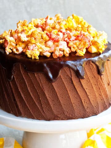 Easy soft and moist chocolate popcorn cake (layer cake) with chocolate buttercream frosting and chocolate ganache on white cake stand.