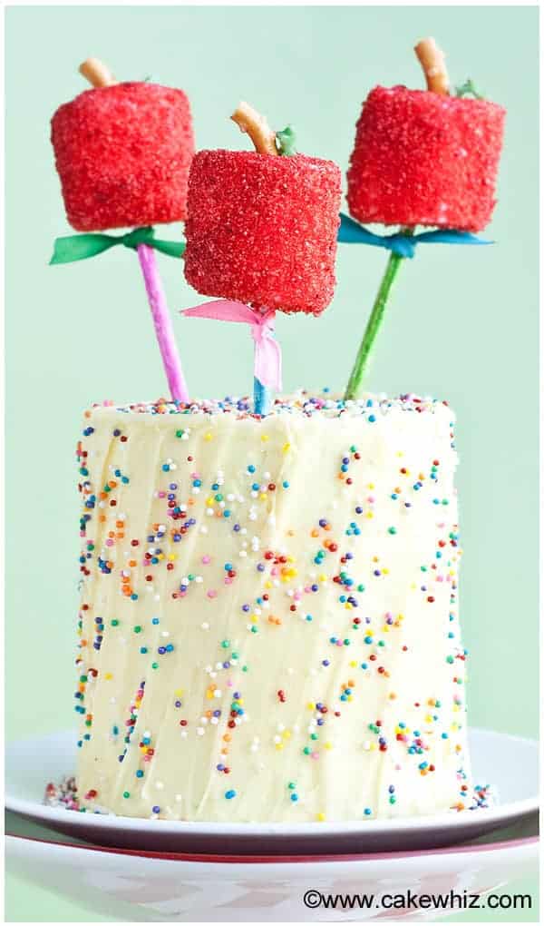 Iced Yellow Cake With Sprinkles That's Topped With Marshmallow Apples on White Dish