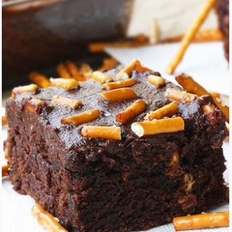 Slice of Easy Cake Mix Brownies With Ganache and Pretzel Topping on White Dish.