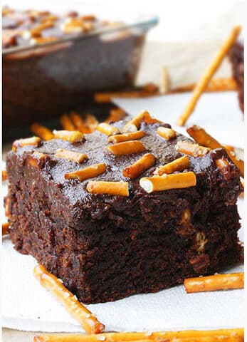 Slice of Easy Cake Mix Brownies With Ganache and Pretzel Topping on White Dish.