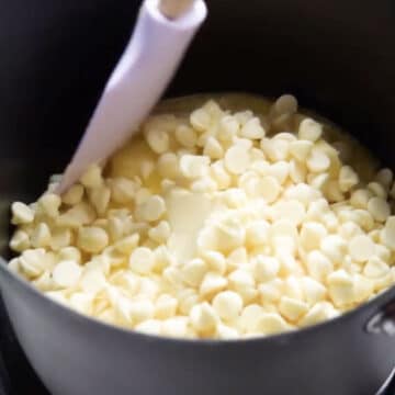White chocolate chips and butter in black nonstick saucepan. 