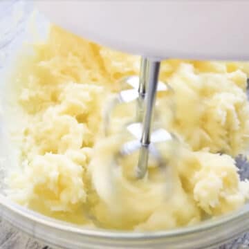 Butter and white chocolate being whipped in glass bowl.