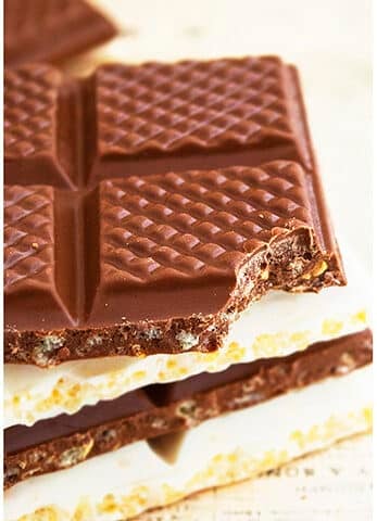 Stack of Easy Chocolate Crunch Bars With One Partially Eaten on Light Brown Background.