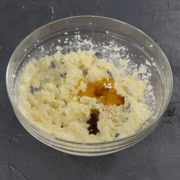 Extracts and egg yolks added to creamed butter sugar mixture in glass bowl. 