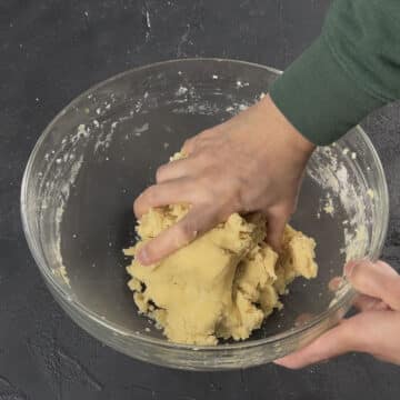 Cookie dough being kneaded with hands. 