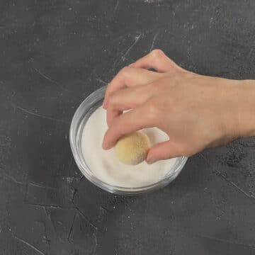 Cookie dough balls being rolled in granulated sugar. 