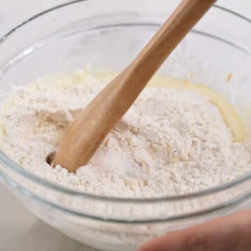Dry flour mixture added to wet mixture and being mixed with a wooden spoon. 