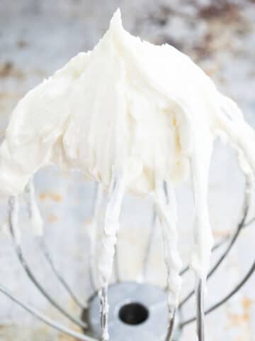 Best Easy White Stable Cream Cheese Frosting on Whisk Placed on Rustic Metal Tray.