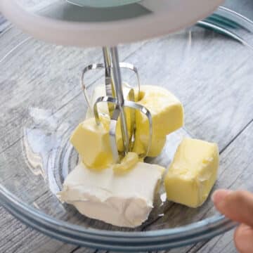 Butter and cream cheese in glass bowl ready to be mixed with hand held mixer. 
