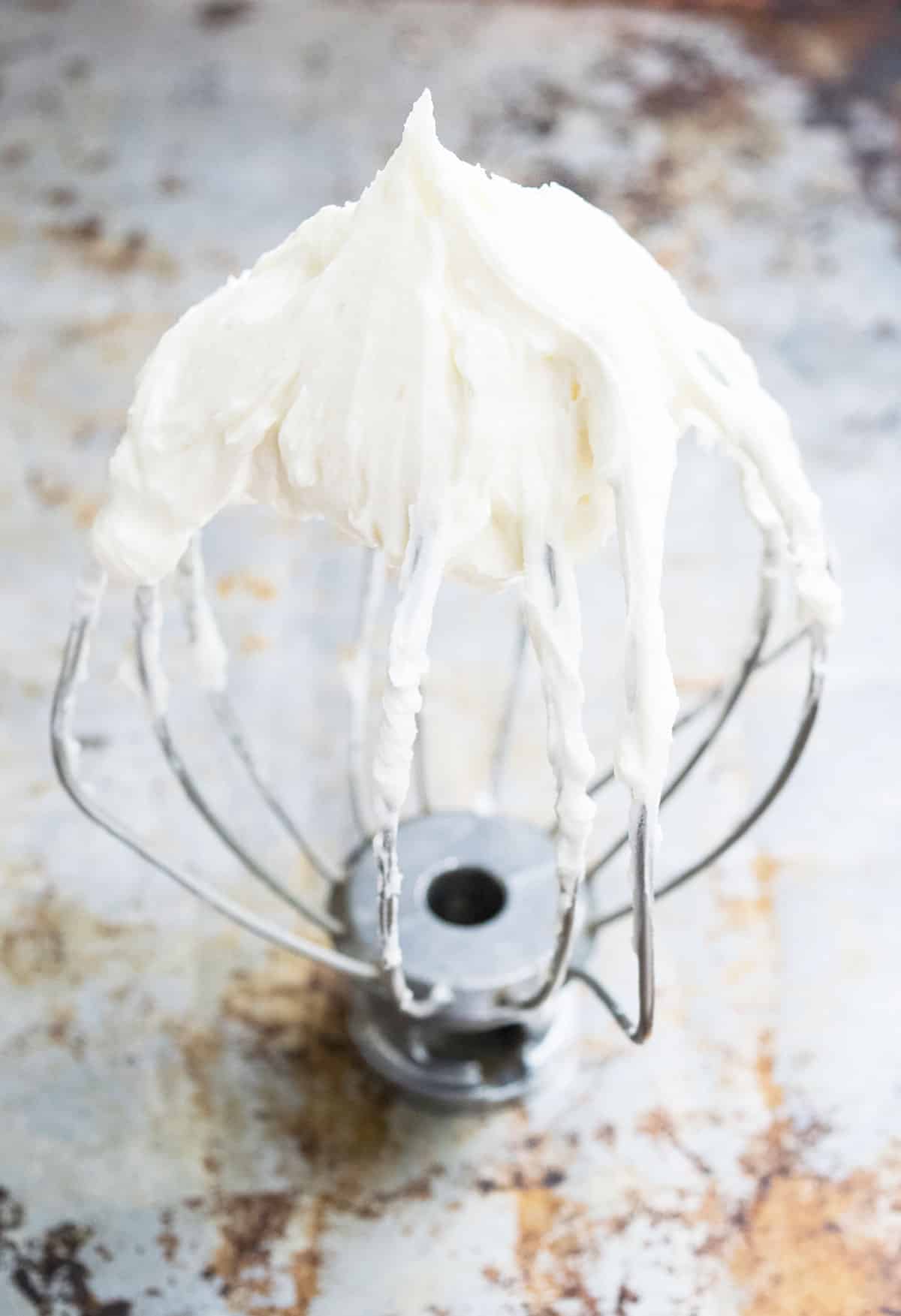 Closeup shot of stable icing on whisk placed on a rustic metal tray. 