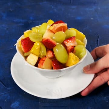 Fruits being served in a white bowl on blue background.