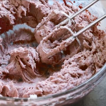 Hand held mixer being used to mix ingredients in glass bowl. 