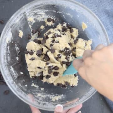 Chocolate chips being mixed into the dough with a rubber spatula.