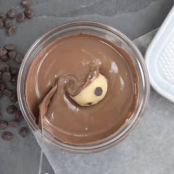 Chilled dough ball being dipped in melted chocolate.