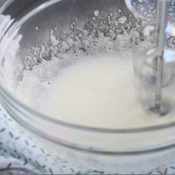 Meringue powder and water being mixed together in a glass bowl. 