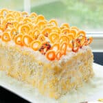 Easy Homemade Soft Mango Cake With Mango Frosting and Chocolate Decorations on White Dish Near Window.