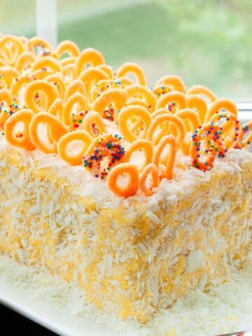 Easy Homemade Soft Mango Cake With Mango Frosting and Chocolate Decorations on White Dish Near Window.