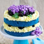 Easy two layer homemade naked cake with yellow buttercream frosting and decorated with flowers and berries.