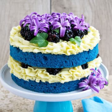 Easy two layer homemade naked cake with yellow buttercream frosting and decorated with flowers and berries.