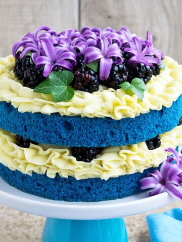 Easy two layer homemade naked cake with yellow buttercream frosting and decorated with flowers and berries.