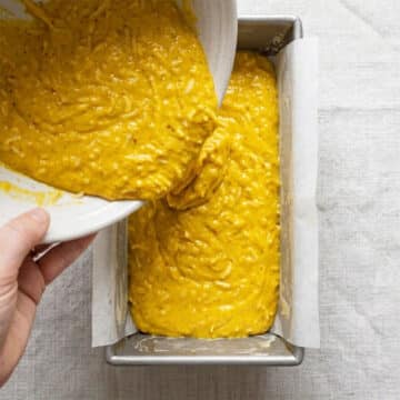Cake batter being poured in lined loaf pan. 