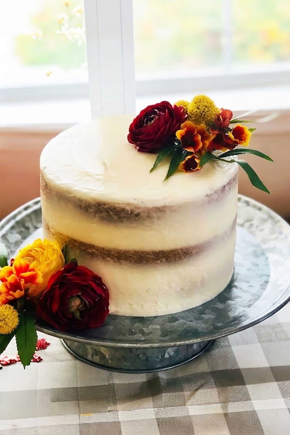 Semi frosted vanilla cake with white buttercream frosting and colorful flowers on rustic stand.