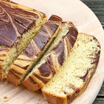 Slices of easy, soft and moist avocado cake with chocolate swirls (marble loaf) on round wood dish.