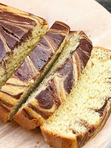 Slices of easy, soft and moist avocado cake with chocolate swirls (marble loaf) on round wood dish.