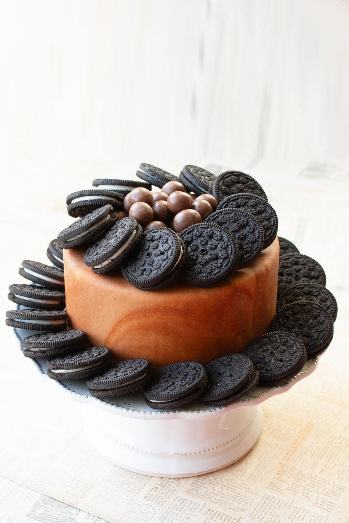 Brown Marble Fondant Cake Decorated With Oreos and Whopper Candies on White Cake Stand. 