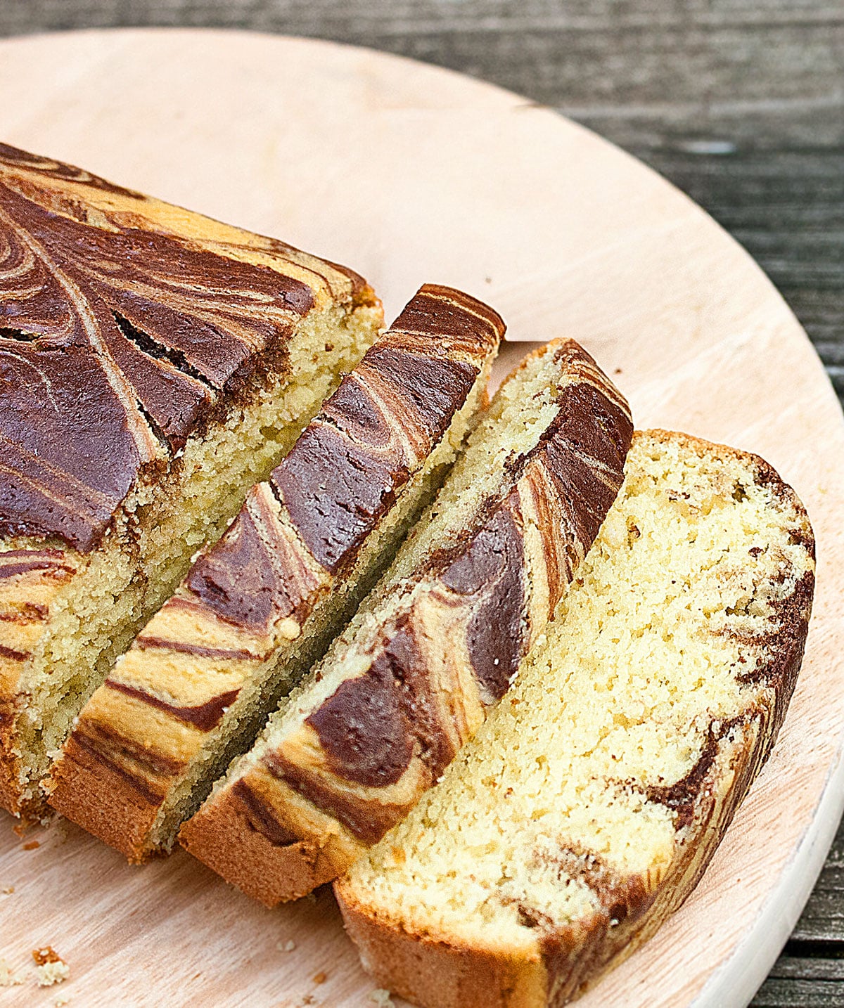 Slices of easy, soft and moist avocado cake with chocolate swirls (marble loaf) on round wood dish. 