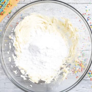 Powdered sugar added to creamed butter in glass bowl. 