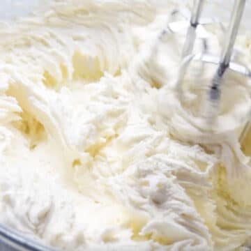 Frosting ingredients being whipped with hand-held mixer. 