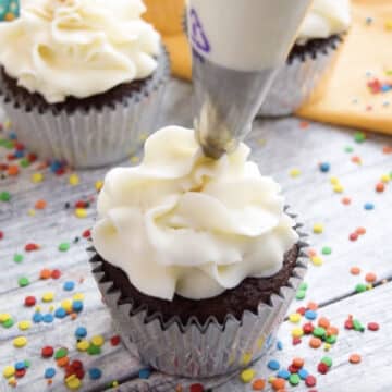 Piping white icing on top of cupcake.