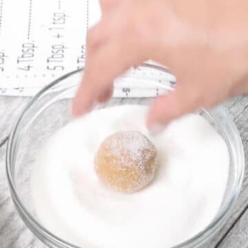 Dough balls being rolled in bowl of granulated sugar. 