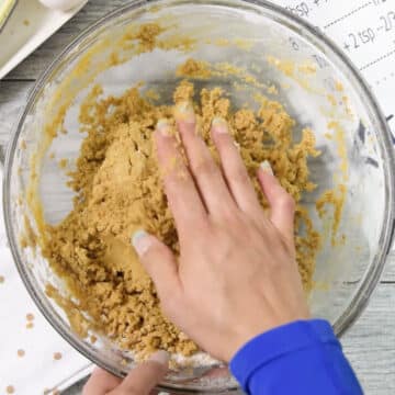 Hands being used to knead cookie dough in glass bowl. 