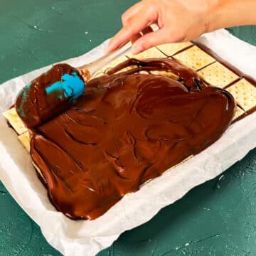 Additional melted chocolate being spread on top of saltine crackers. 