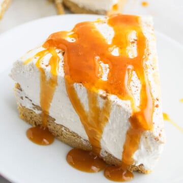 Slice of No Bake Eggnog Cheesecake With Graham Cracker Crust and Caramel Sauce Drizzle on White Dish.