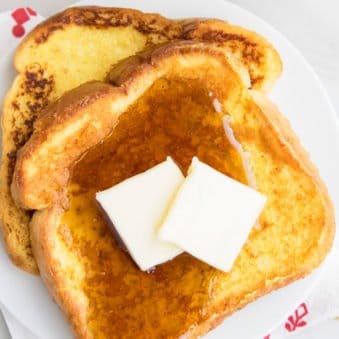 Slices of Easy Eggnog French Toast With Maple Syrup and Butter on White Dish.