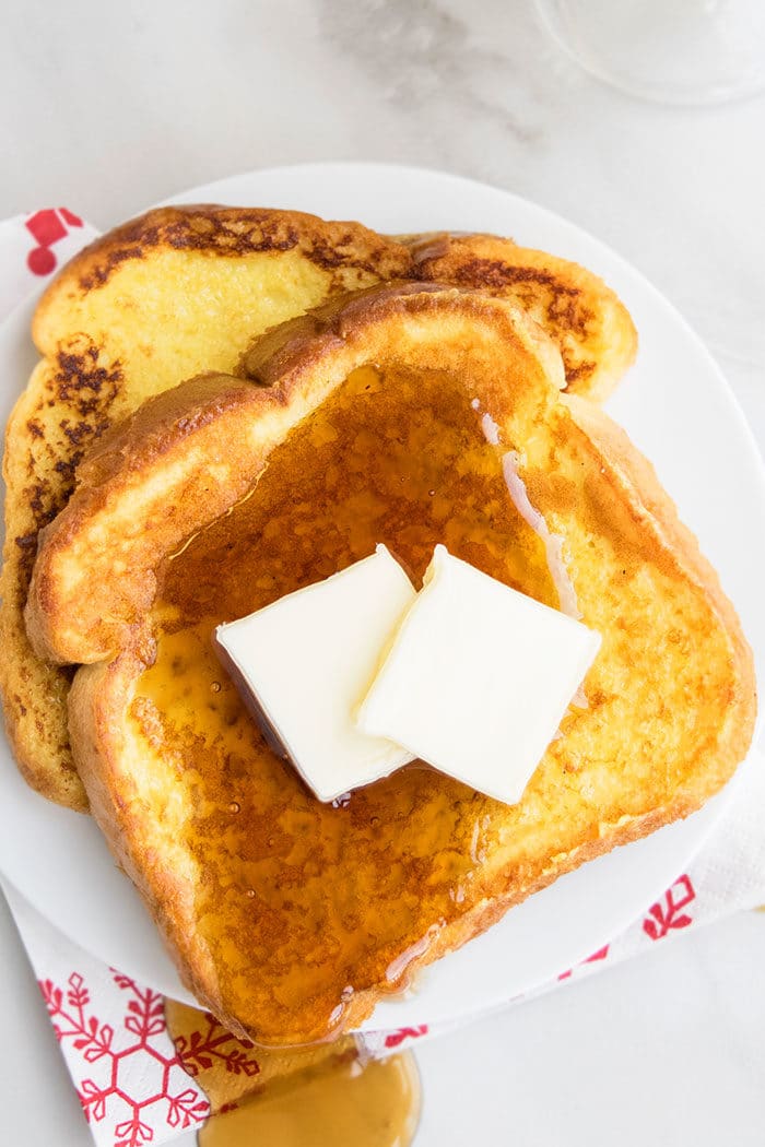 Slices of Easy Eggnog French Toast With Maple Syrup and Butter on White Dish. 