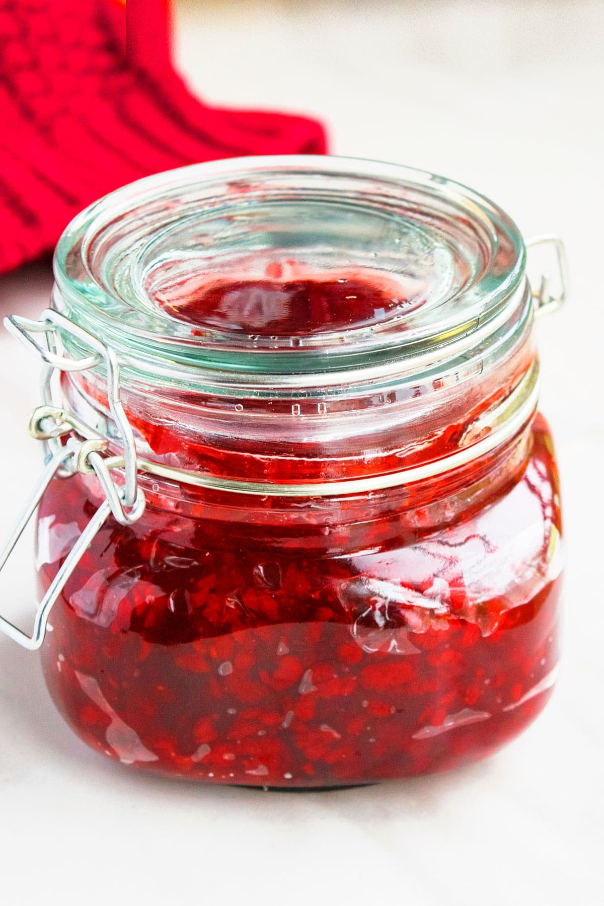 Glass jar of red berry filling on white background. 