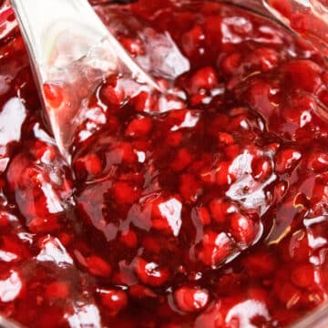 Closeup shot of spoonful of best easy homemade raspberry pie filling with fresh or frozen raspberries in glass jar.