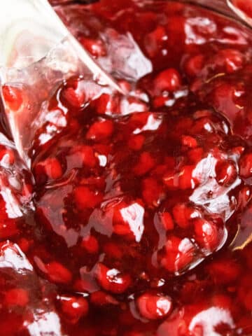 Closeup shot of spoonful of best easy homemade raspberry pie filling with fresh or frozen raspberries in glass jar.