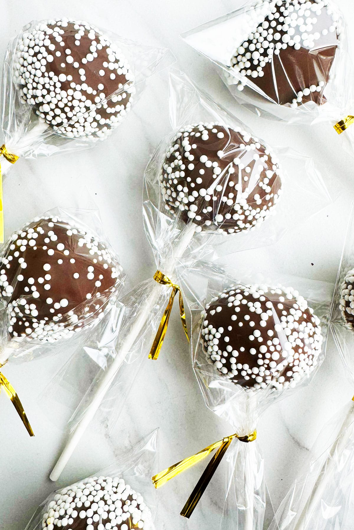 Chocolate pops with white sprinkles covered in plastic bags and golden ties. 
